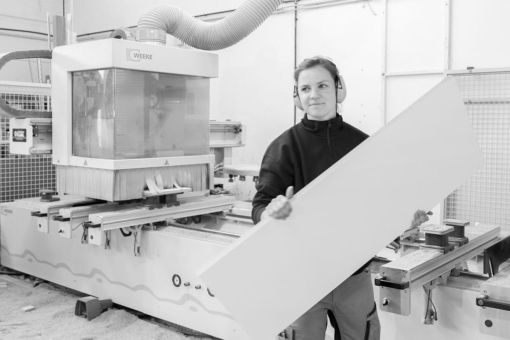 Mitarbeiter in Bergisch Gladbach. Sie schaut in die Kamera und hält ein Brett in der Hand.