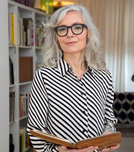 Frau steht im Wohnzimmer und posiert für die Kamera in Oberberg. Sie hält ein Buch in der Hand